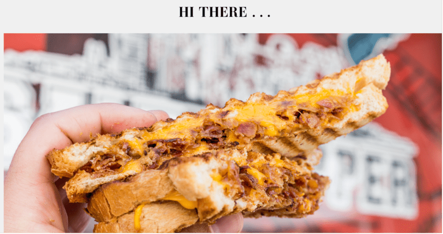 A person holding a grilled cheese sandwich with bacon and cheese. The sandwich is golden brown and looks melted and gooey. The person is smiling and holding up the sandwich for a photo.