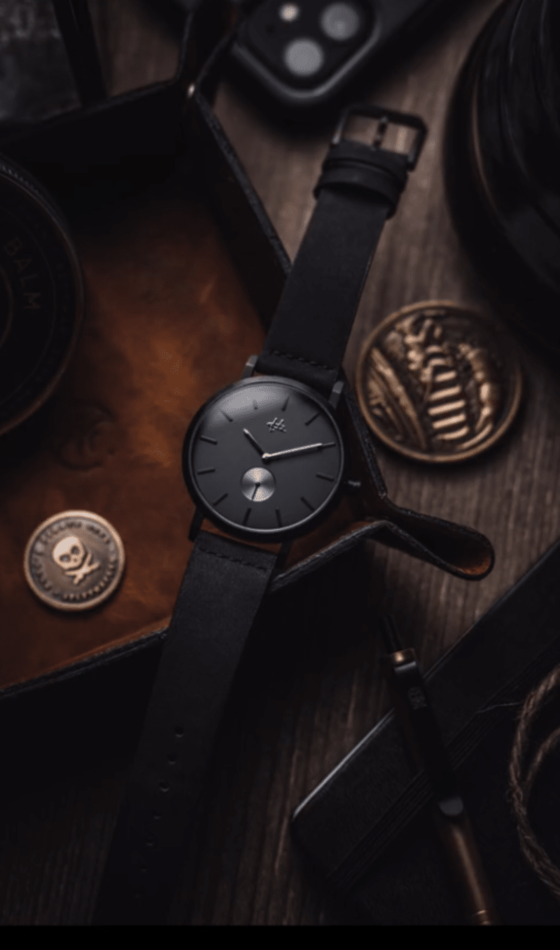 dark, moody pic of a black matte watch on a wooden desk